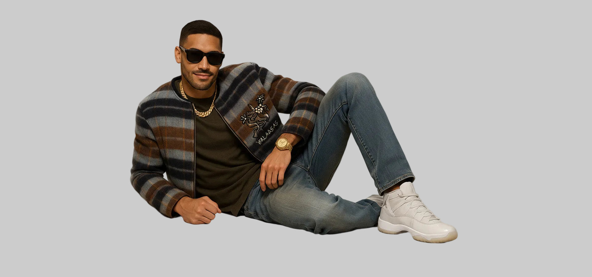 Man sitting on the floor wearing a striped sweater, jeans, and white sneakers against a plain background